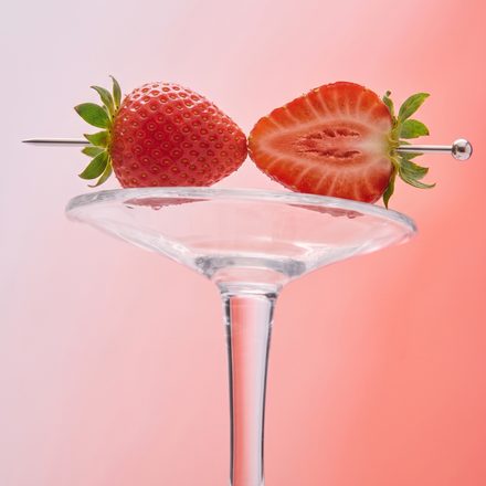 Strawberries resting on the rim of a coupe glass against pink