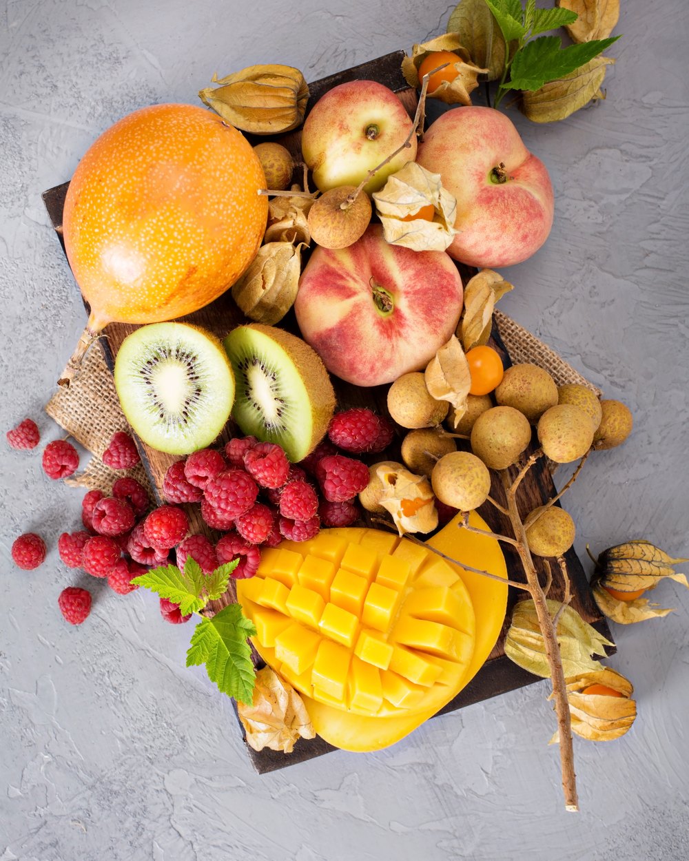 A board of ripe tropical fruit — mango, kiwi, apples, raspberries and longan