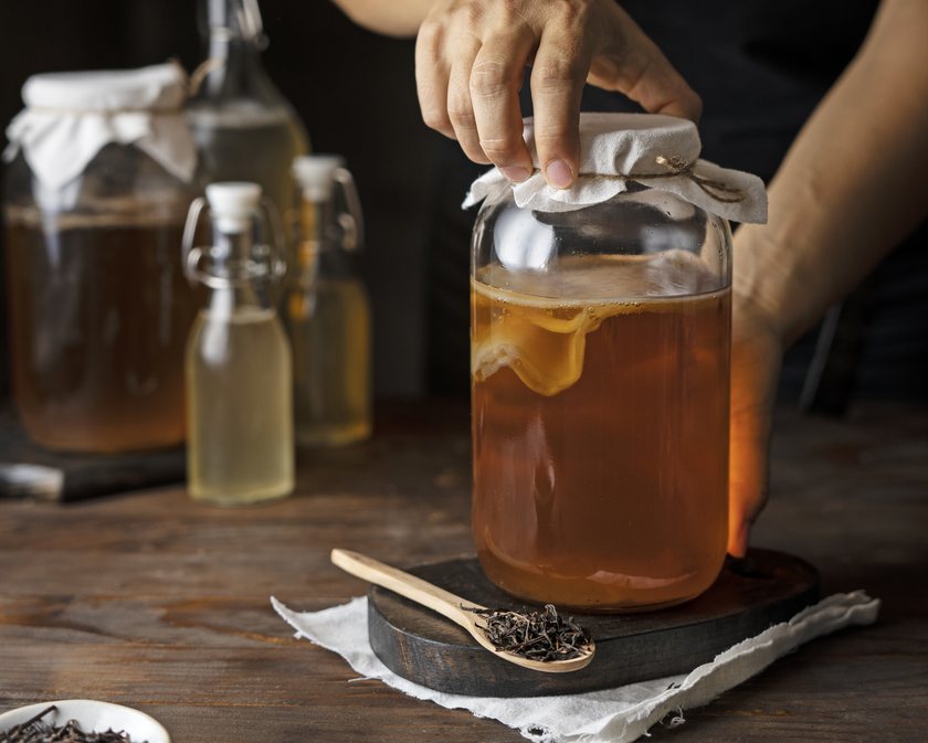 A maker lifting the cloth cover from a jar of live kombucha culture