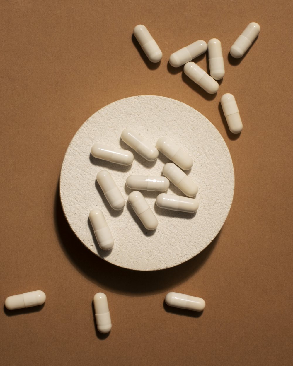 Probiotic capsules scattered across a plate on a brown backdrop